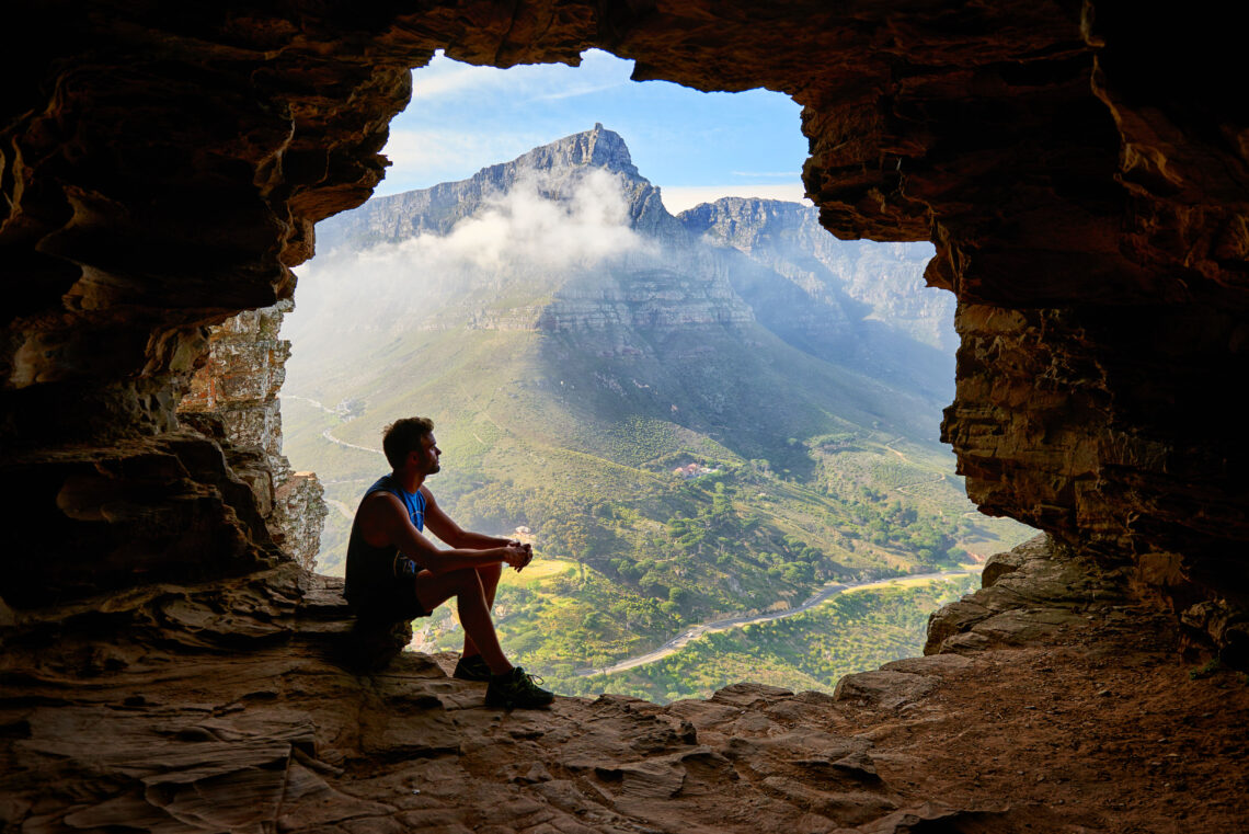 A man looking at a mountain from a cave.