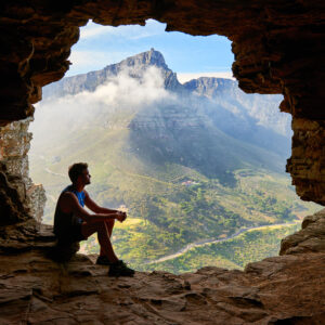 A man looking at a mountain from a cave.