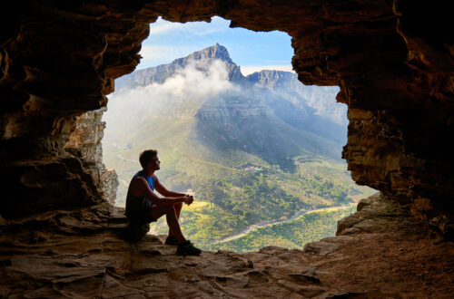 A man looking at a mountain from a cave.