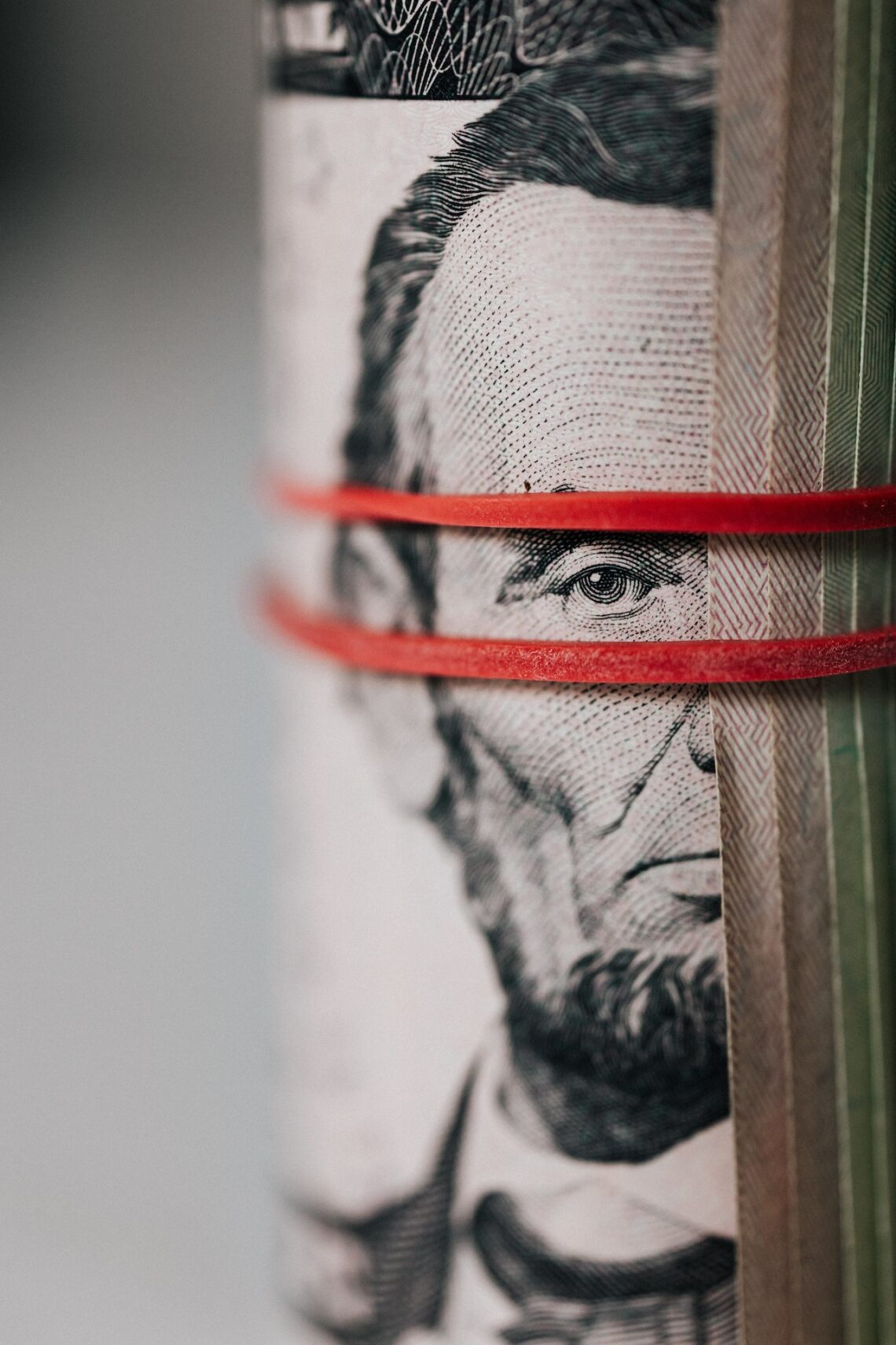 A furled banknote showing Abe Lincoln peeping through two red rubber bands.