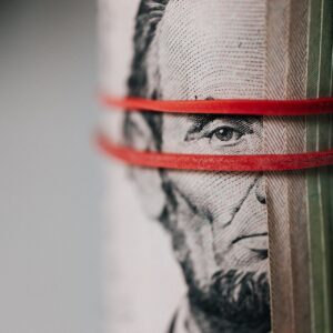 A furled banknote showing Abe Lincoln peeping through two red rubber bands.