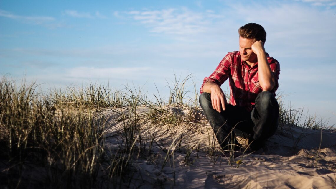 A man sitting at a cliff's edge and looking confused