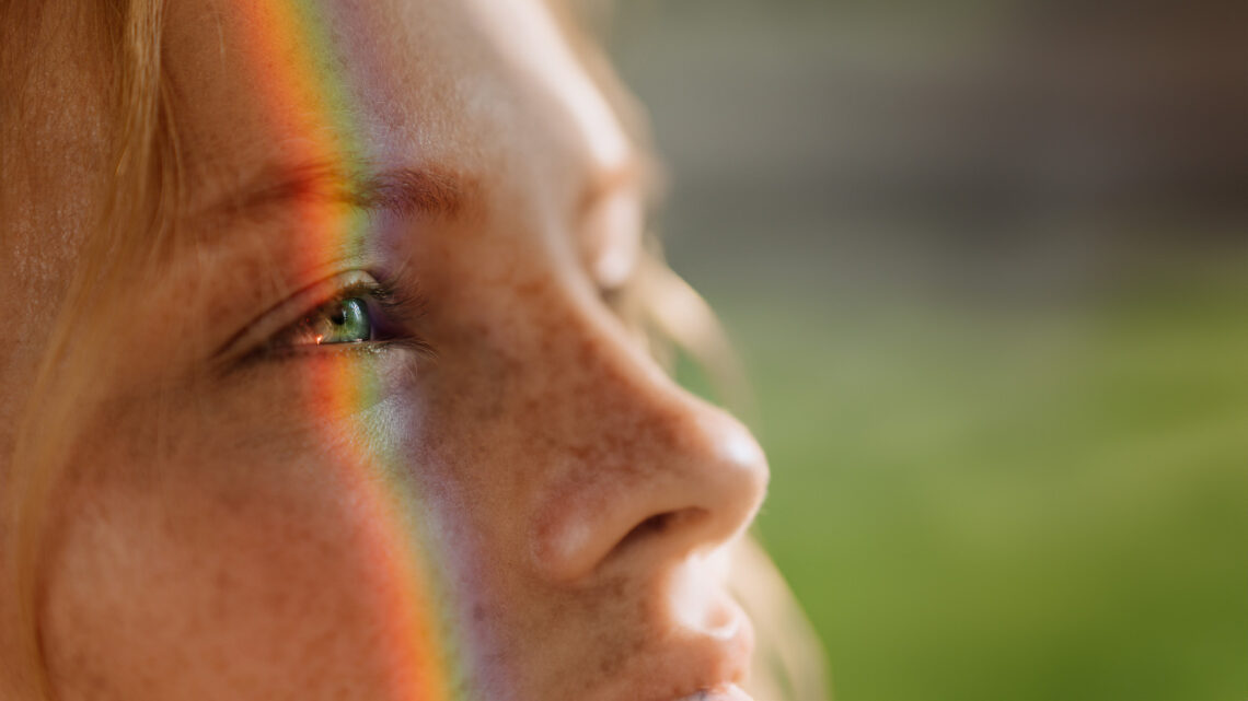 A girl's face with a rainbow prism projected upon it.