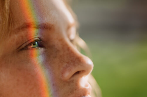 A girl's face with a rainbow prism projected upon it.