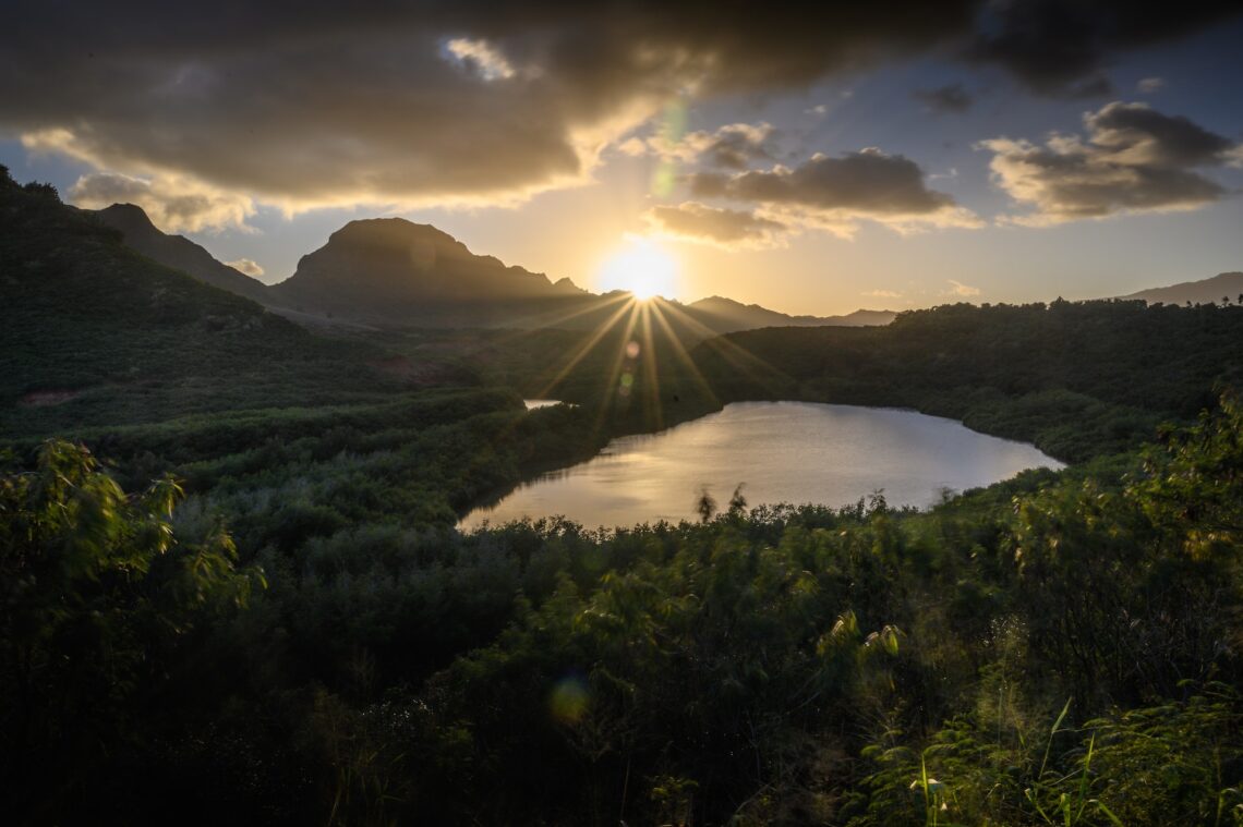 An image of the sun peeping through the clouds above a Hawaiian lake.