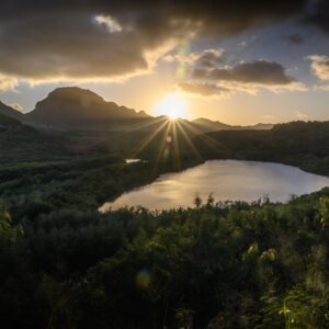 An image of the sun peeping through the clouds above a Hawaiian lake.